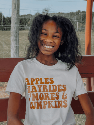 Girl wearing fall shirt that says Apples, Hayrides, S'mores and Pumpkins