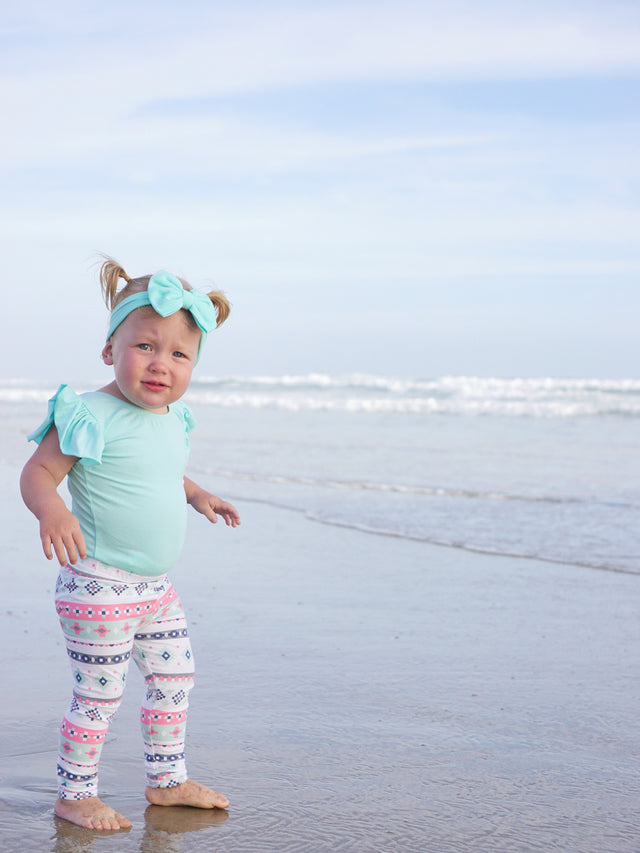 Little girl on beach wearing pastel aztec leggings with mint green shirt