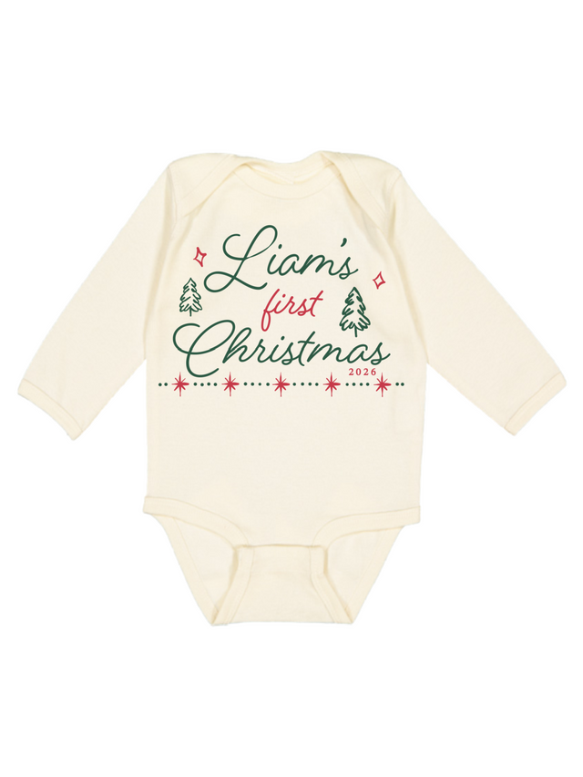 An off-white long-sleeve baby bodysuit with a festive Christmas graphic on the front reading 'Liam's first Christmas 2023' in green and red lettering with small tree and star illustrations.