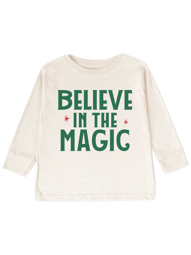An off-white long-sleeve t-shirt with 'BELIEVE IN THE MAGIC' printed in green and red on the front, displayed against a solid white background.