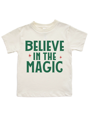 An off-white short-sleeve t-shirt with the phrase 'BELIEVE IN THE MAGIC' printed in dark green block letters, accented with small red starbursts, shown against a plain white background.