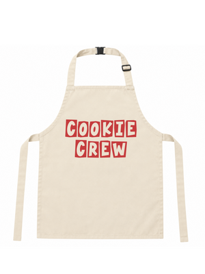 An off-white canvas apron with 'COOKIE CREW' printed in red block letters with white outlines across the chest, featuring a neck strap and waist ties.