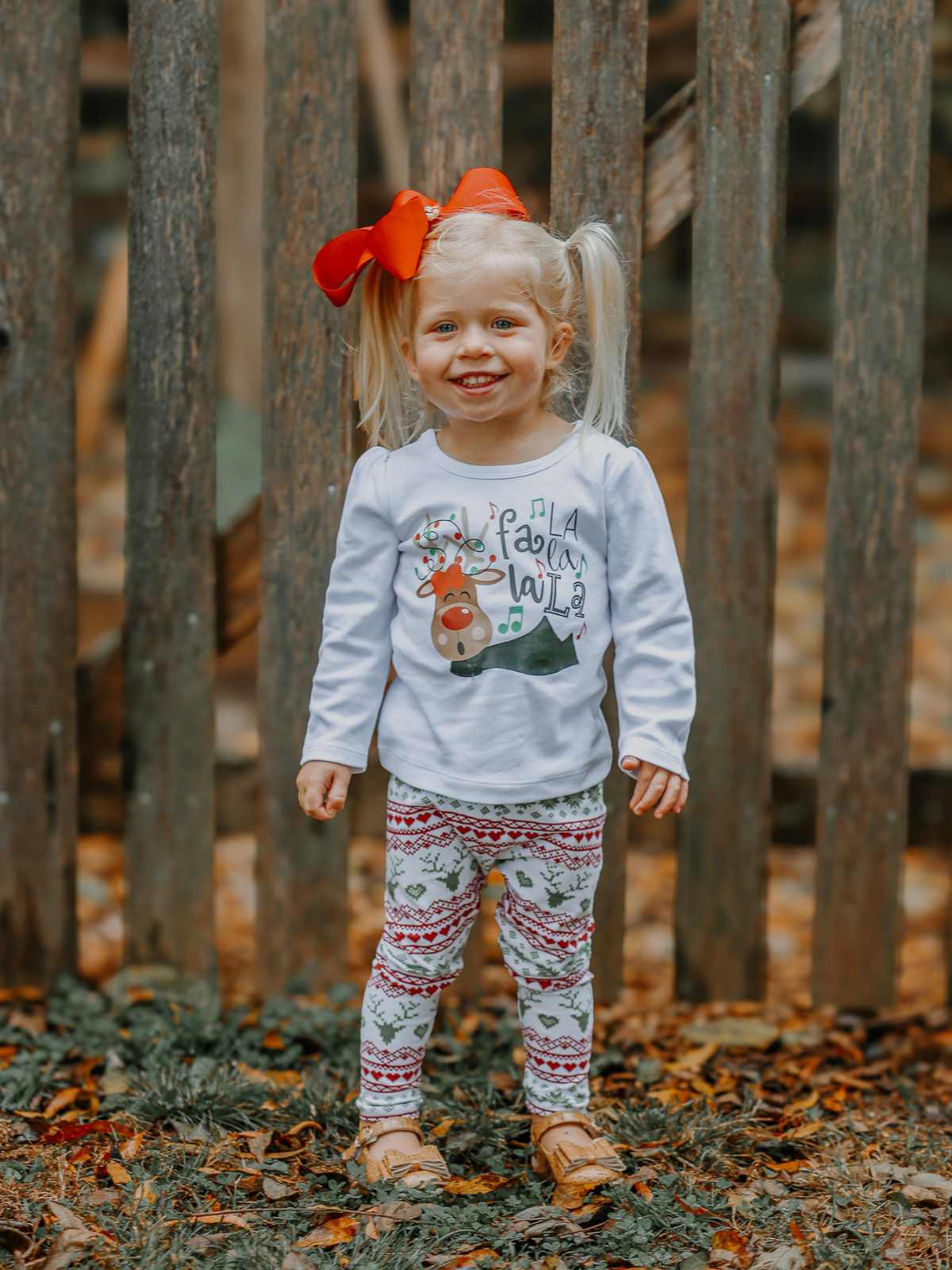 Young girl wearing white long sleeve shirt with reindeer singing Fa la la la and Christmas leggings