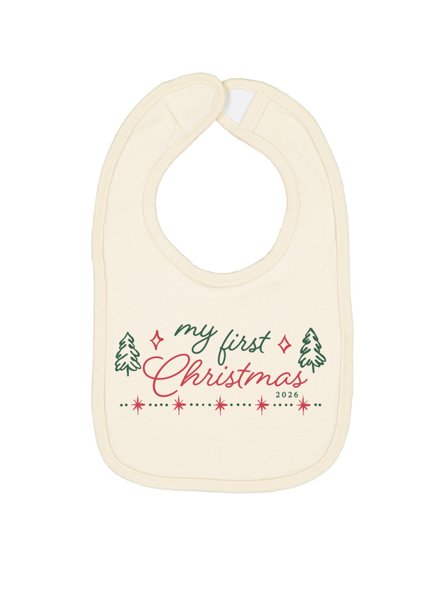 An off-white baby bib with a 'my first Christmas 2026' graphic printed on the front, featuring green and pink text and festive illustrations, set against a plain white background.
