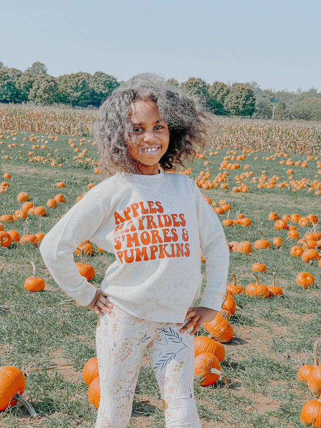 Young girl in pumpkin patch wearing leggings and fall themed sweatshirt