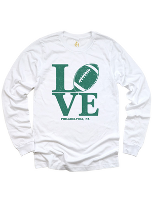 A white long-sleeve t-shirt with a green graphic on the front that spells 'LOVE' using a football and the word 'LOVE', with 'PHILADELPHIA, PA' printed below.