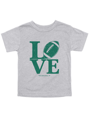 A toddler heather gray t-shirt featuring a green graphic that spells 'LOVE' with a football representing the letter 'O', and 'PHILADELPHIA, PA' printed below.