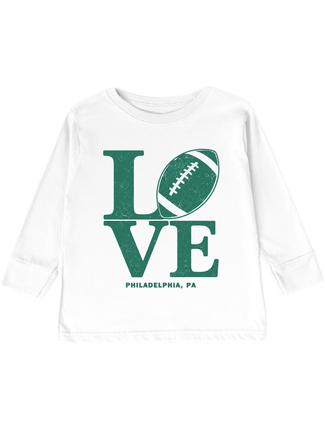A white long-sleeve toddler or youth T-shirt with a distressed green graphic on the front. The graphic spells 'LOVE' using a football as the letter 'O', with 'PHILADELPHIA, PA' printed below in smaller green text.