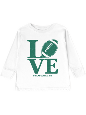 A white long-sleeve toddler or youth T-shirt with a distressed green graphic on the front. The graphic spells 'LOVE' using a football as the letter 'O', with 'PHILADELPHIA, PA' printed below in smaller green text.
