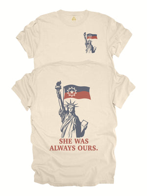 Lady Liberty Juneteenth adult shirt in cream with front pocket-style flag graphic and back design reading “She Was Always Ours.”