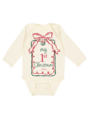 An off-white long-sleeve baby bodysuit featuring a Christmas gift tag graphic on the front with a red bow, green border, and the text 'my 1st Christmas 2026'.