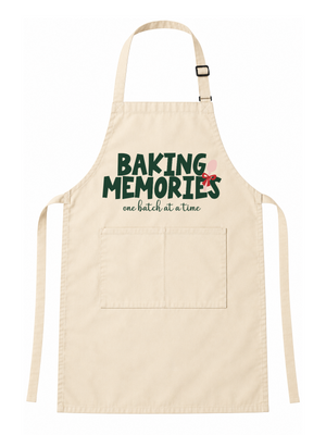 A light beige fabric apron with a front pocket, featuring the printed text 'BAKING MEMORIES one batch at a time' in dark green and pink on the chest, displayed against a solid white background.