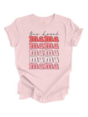 Soft pink "One Loved Mama" Valentine's Day shirt featuring a retro stacked text design in pink and red hues, crafted from cotton with a unisex fit.