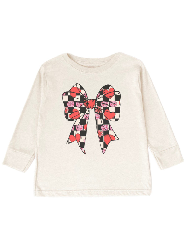 Natural-colored long sleeve girls Valentine shirt featuring a retro Coquette Bow design with checkered hearts, pink dice, and flowers, displayed flat on a white background.