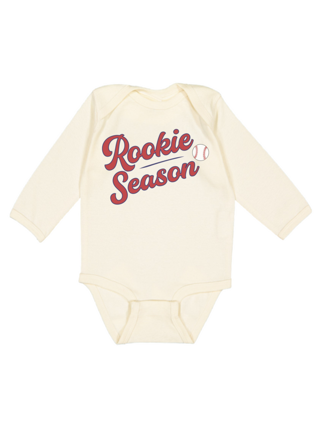 A cream-colored long-sleeve baby bodysuit featuring 'Rookie Season' printed in red script across the chest, accompanied by a small baseball graphic.