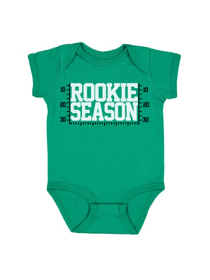 A green short-sleeve baby bodysuit with a white and black 'ROOKIE SEASON' graphic printed on the chest, displayed against a solid white background.