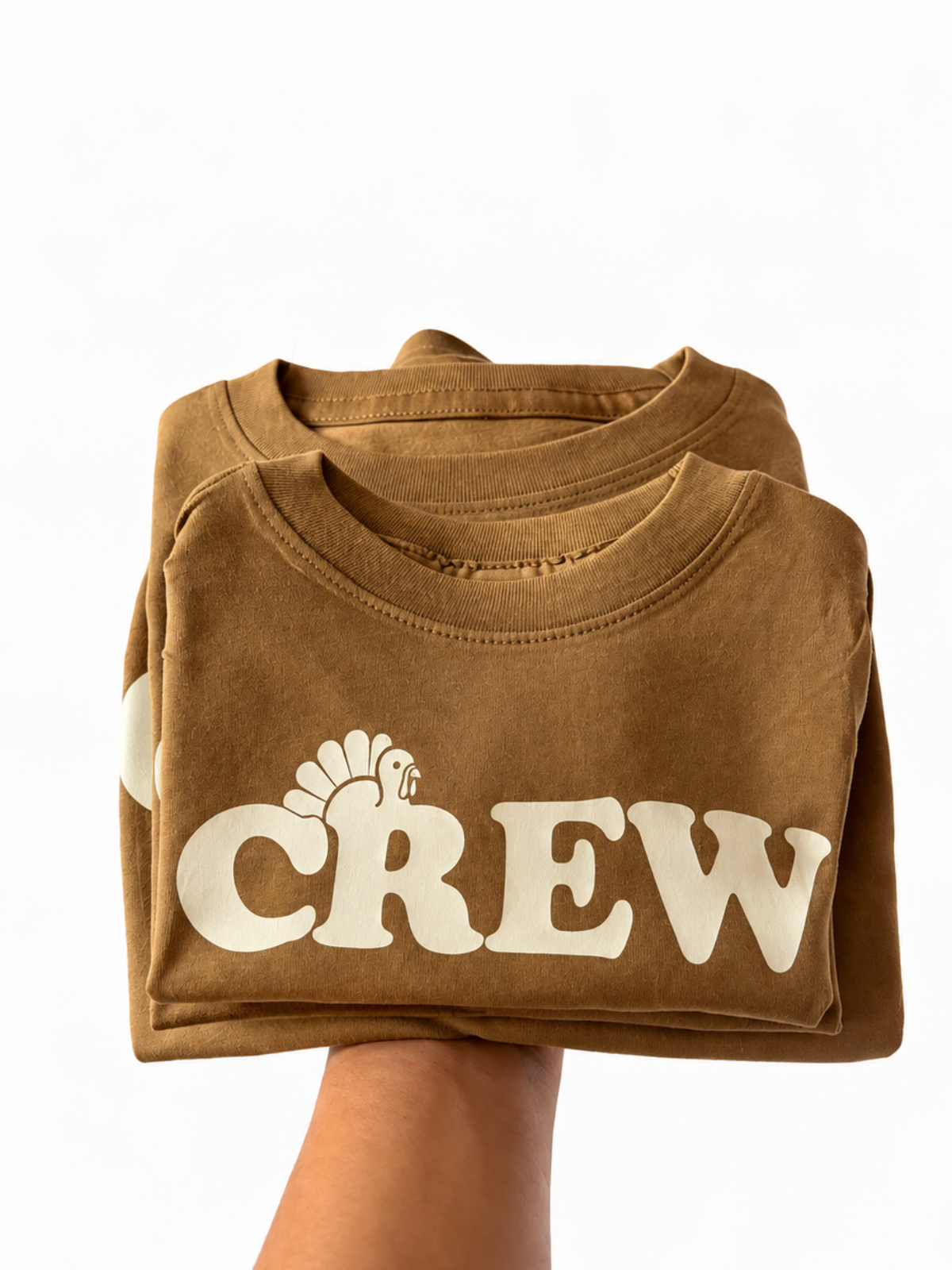 Hand holding stack of brown shirts that read CREW with a turkey