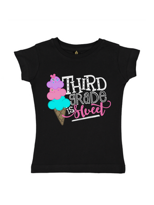 A black short-sleeve t-shirt for kids, featuring a colorful graphic on the front with an ice cream cone and the text 'THIRD GRADE IS Sweet' in white, pink, and turquoise lettering.