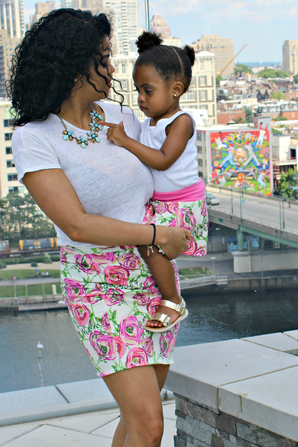 Mom and daughter wearing matching floral skirts—mom in a pencil skirt, daughter in a circle skirt—walking hand in hand in spring sunshine